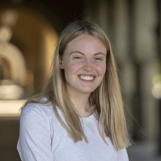 A young woman with straight blonde hair and wearing a white shirt smiles at the camera. She briefly held a record for a famous math problem.